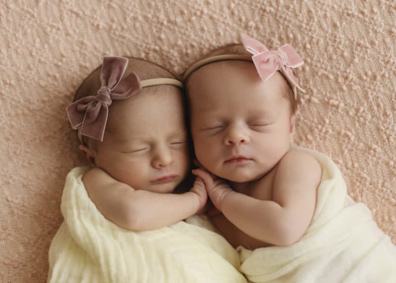 newborn baby twin girls holding hands in a studio photo shoot