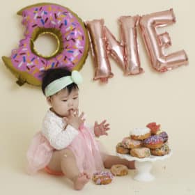 one year old cake smash studio photoshoot with donuts tasting pink sprinkles