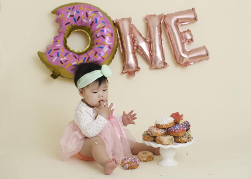 one year old cake smash studio photoshoot with donuts tasting pink sprinkles
