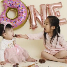 one year old girl and big sister with donuts in a pink studio cake smash session sacramento california