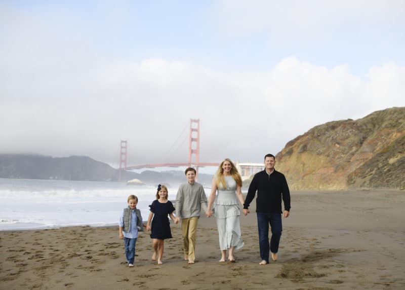 family walking along the beach holding hands in front of the golden gate bridge