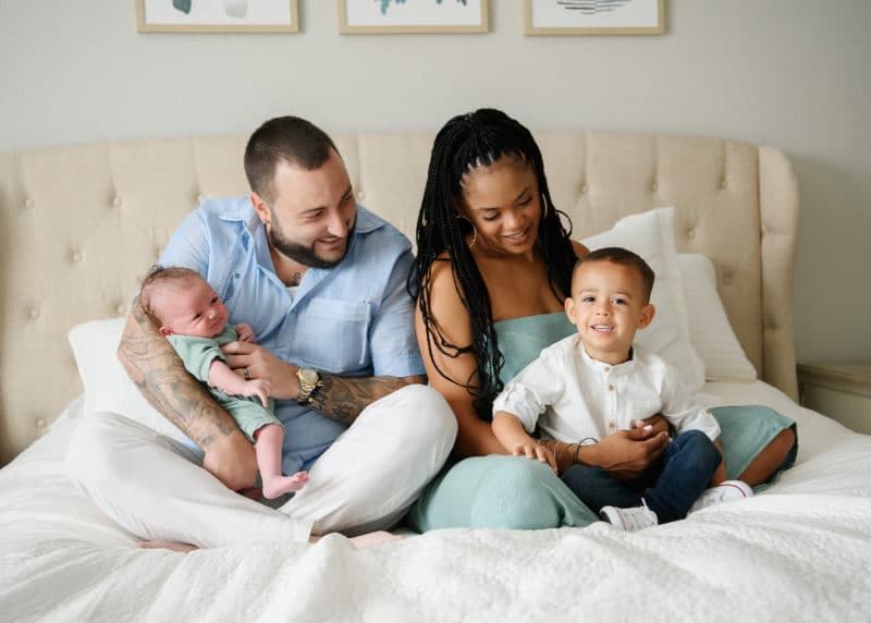 family sitting on bed at-home newborn session sacramento california