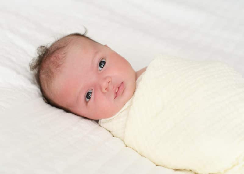 newborn baby boy swaddled in white blanket 