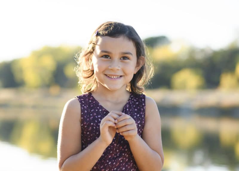 young girl smiling by the river during fall family photos rancho cordova california