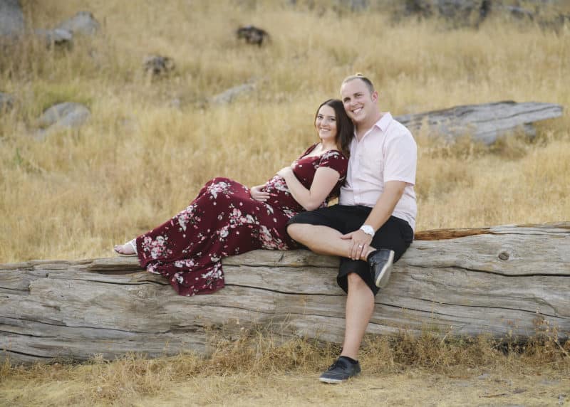 couple sitting on a log maternity photo shoot granite bay california