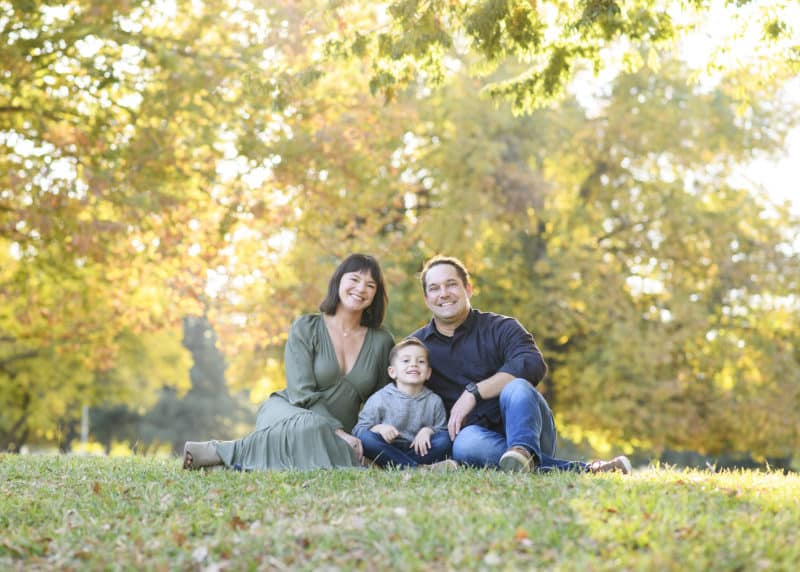 family of three sitting among the fall leaves