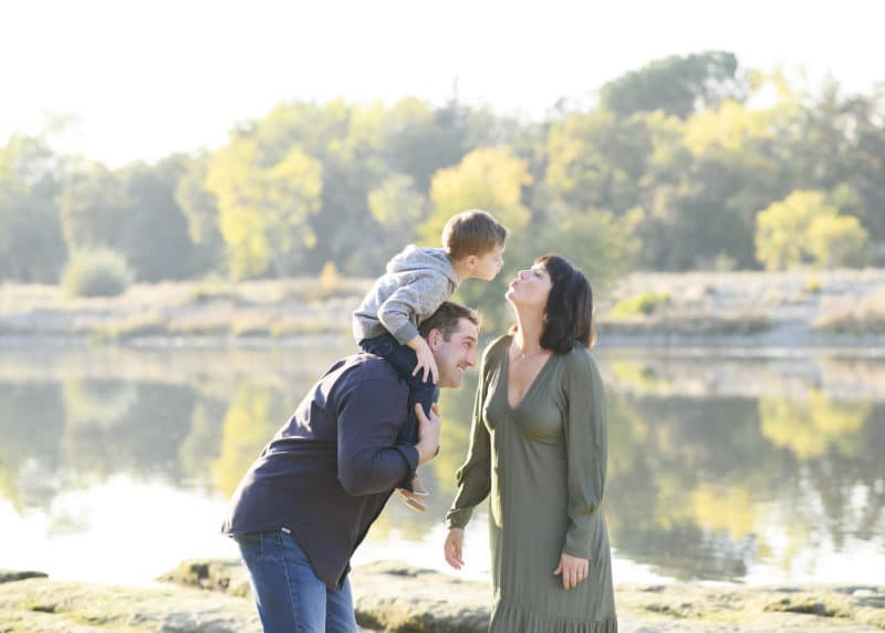 mom and son kissing on dad's shoulders by the river