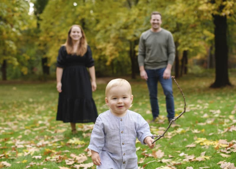 toddler boy holding a stick, mom and dad smiling behind him