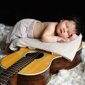 newborn baby boy snuggling with guitar