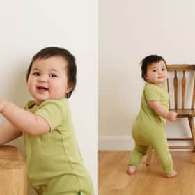 one year old baby girl balancing on chair, smiling