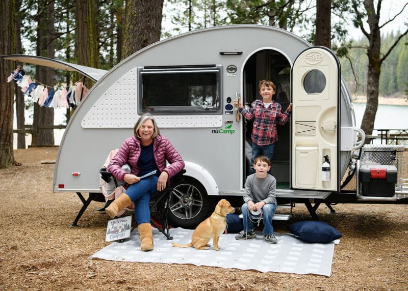mom and two sons posing in front of their camper with family dog