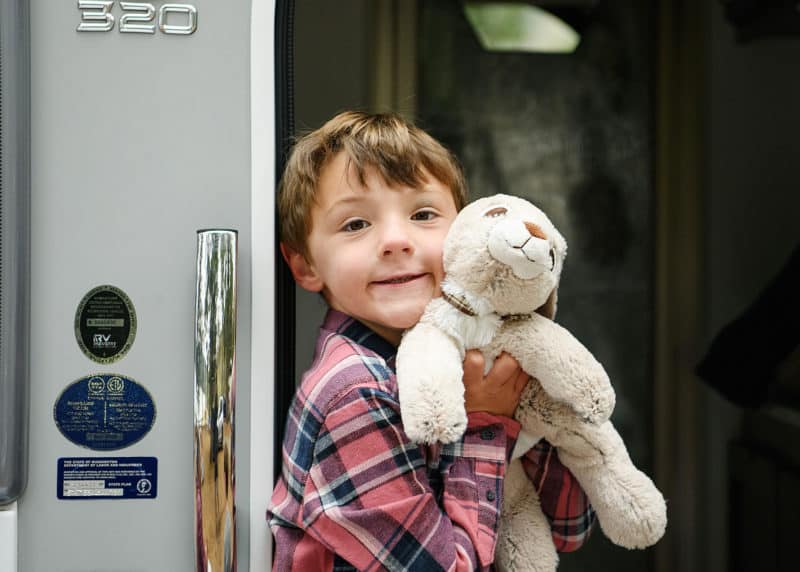 young boy holding stuffed animal in front of family camper