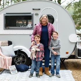 family of three in front of their small camper with the dog