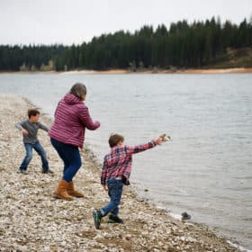 mom and two young sons skipping rocks in the lake