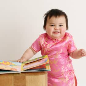 one year old baby girl in traditional dress standing with books