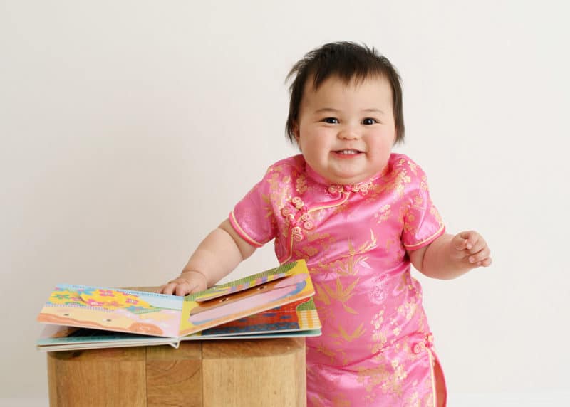 one year old baby girl in traditional dress standing with books