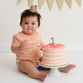 one year old baby girl sitting with smash cake in studio photo shoot