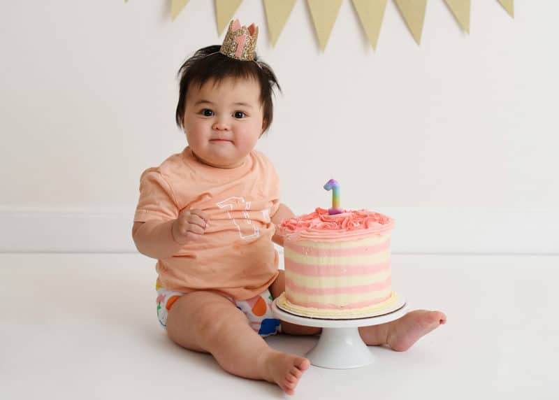one year old baby girl sitting with smash cake in studio photo shoot