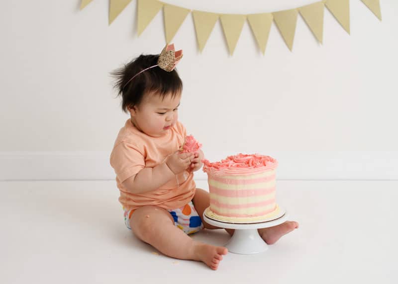 one year old girl looking at smash cake studio shoot