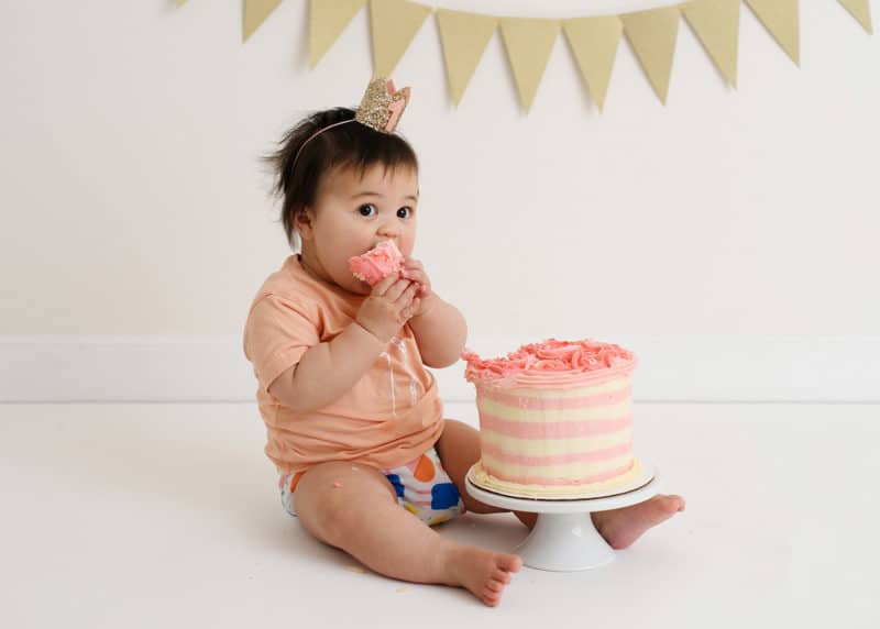 one year old baby girl eating smash cake in studio photo shoot
