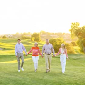 family of four holding hands on the golf course in the sunlight
