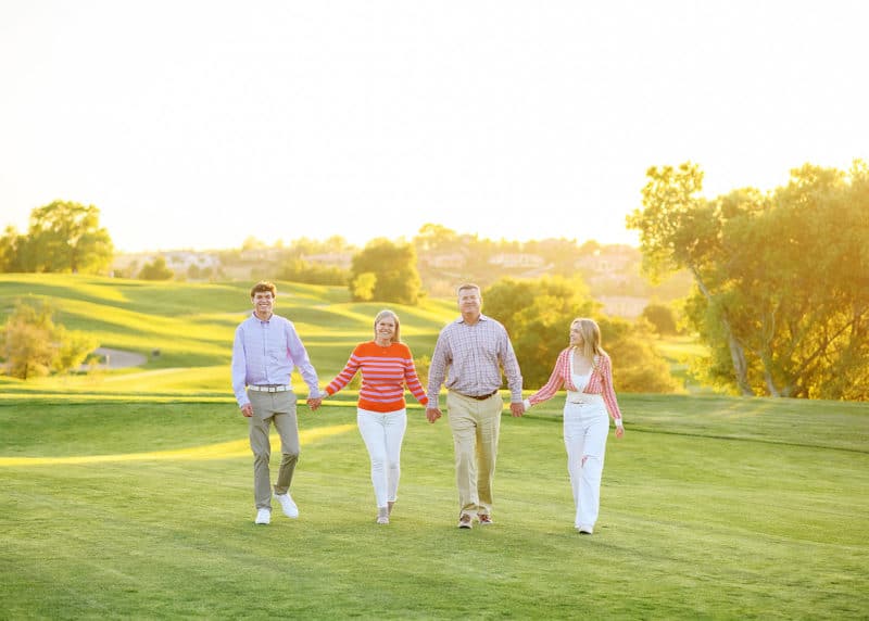 family of four holding hands on the golf course in the sunlight