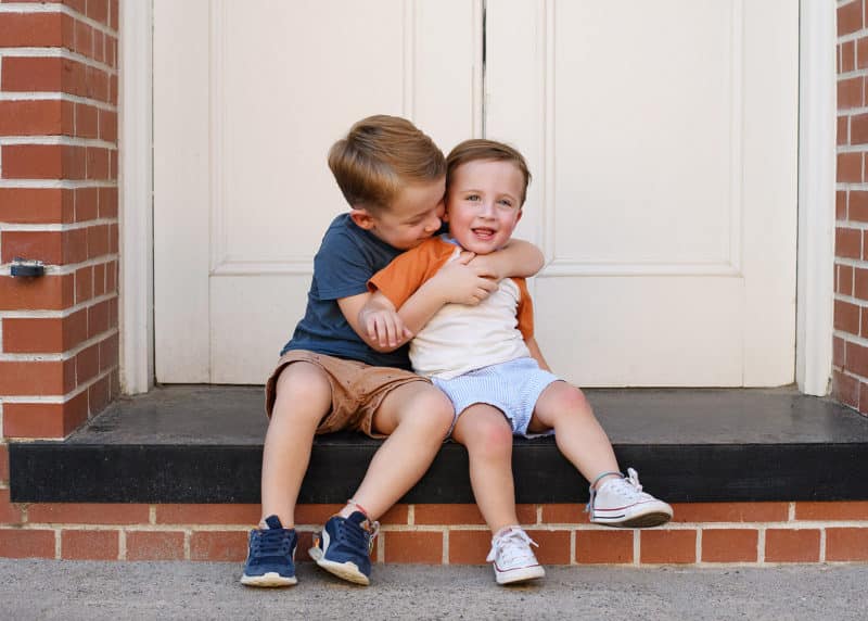 two brothers hugging and smiling in front of a brick building in old sacramento california