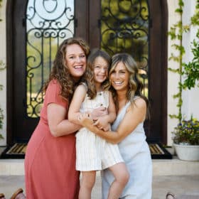 aunts posing with young girl in front of ornate door with spring foliage