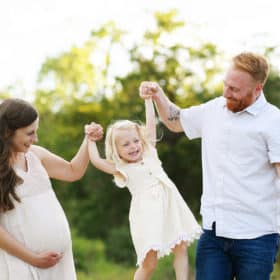 pregnant mom and dad swinging toddler girl during maternity photo session