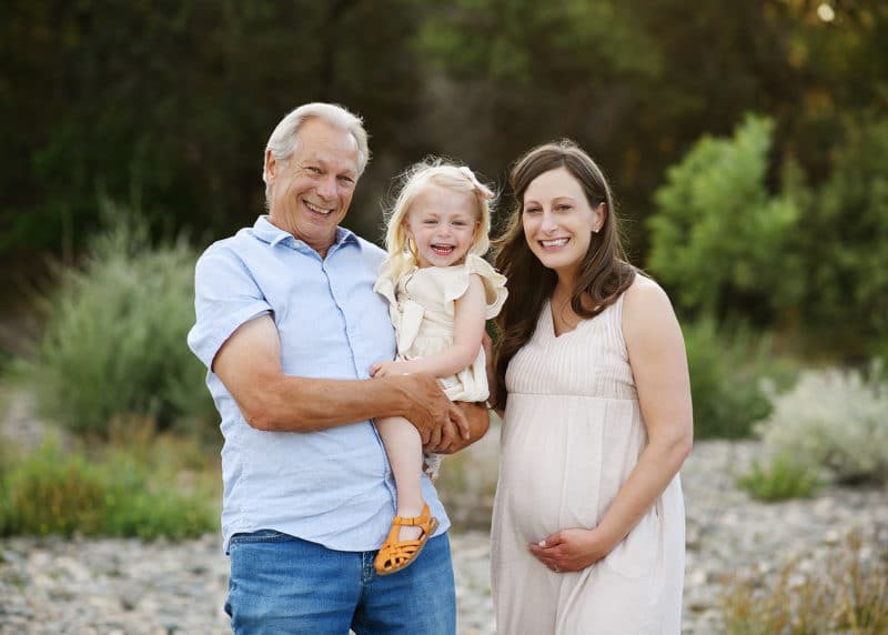 pregnant woman with dad and daughter posing by the river