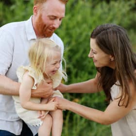 mom tickling young daughter with dad holding her