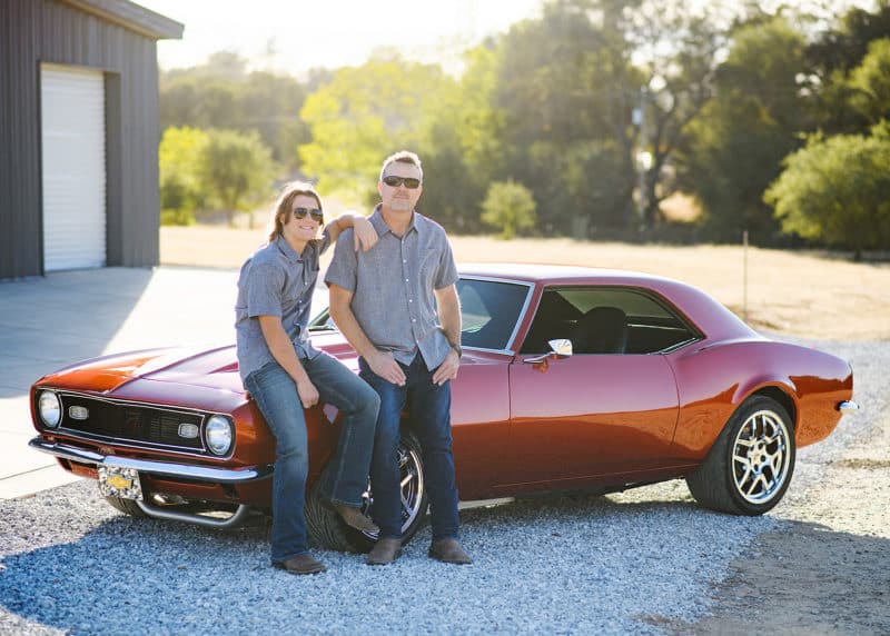 father and son posing together in front of garage with old chevy camero