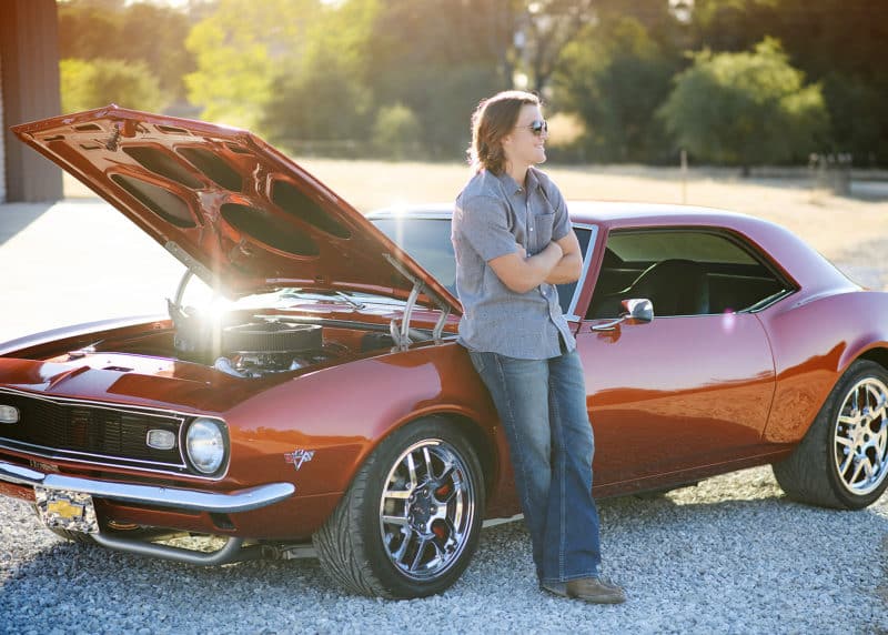 teenage son posing by classic chevy camero with engine popped natural sunlight
