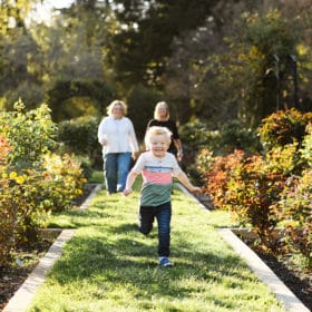 young boy running in the garden with moms following behind