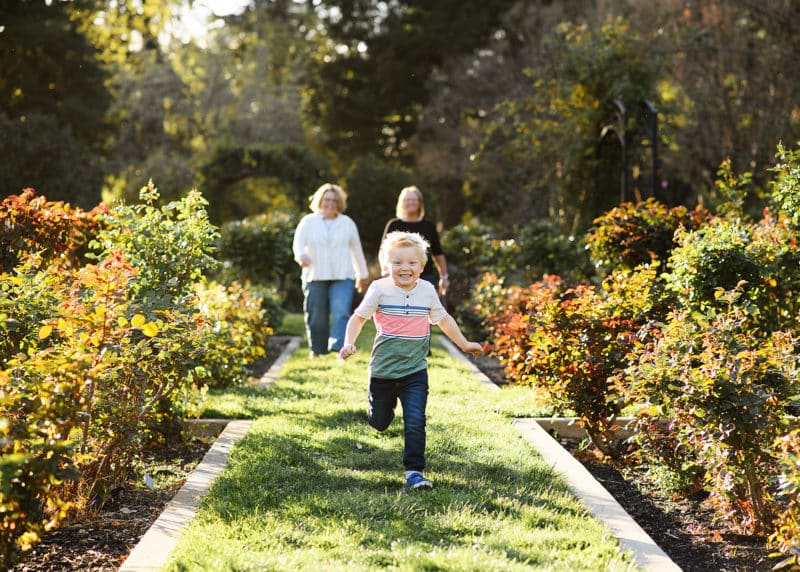 young boy running in the garden with moms following behind