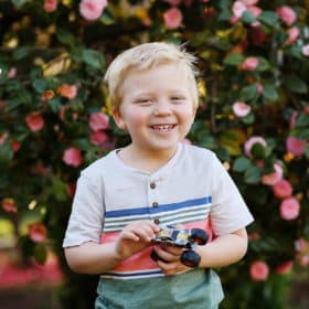 young boy laughing in front of spring flowers with toy car