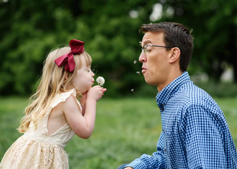 young girl blowing dandelion in dad's face funny sacramento california