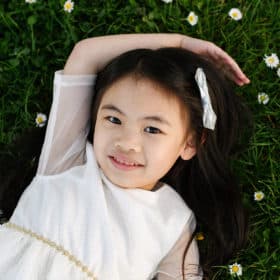 young girl laying in the grass with flowers outside