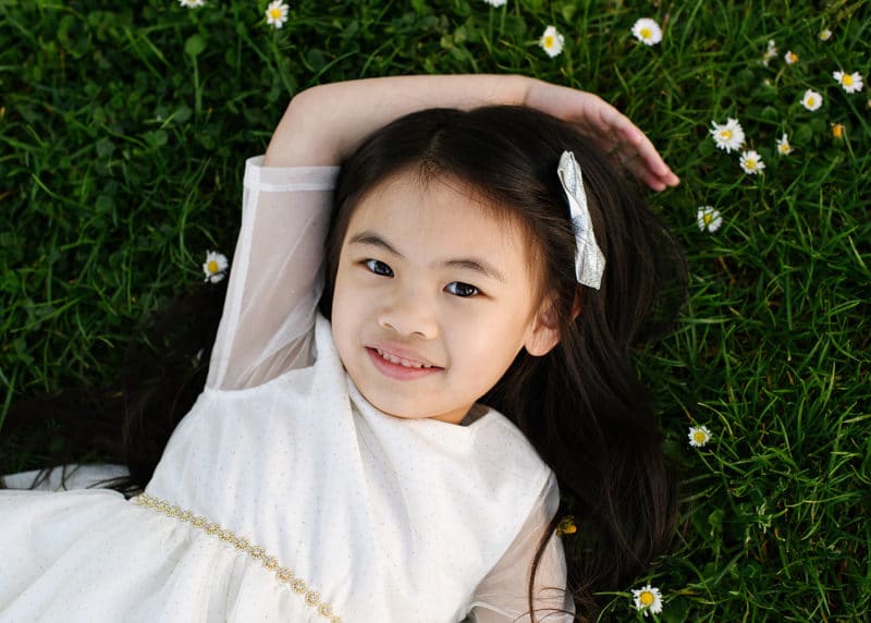 young girl laying in the grass with flowers outside