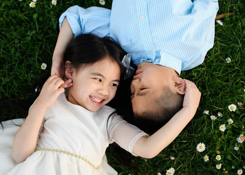 brother and sister laughing together on the grass surrounded by small flowers