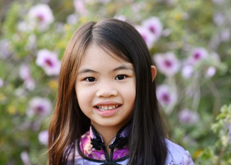 young girl smiling in front of floral bush outside in sacramento california
