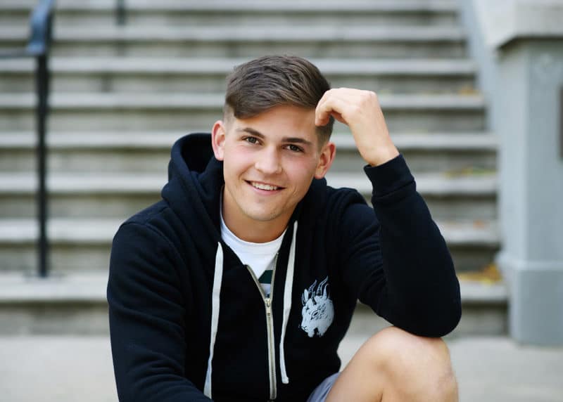 high school boy sitting on concrete steps with a black sweatshirt on