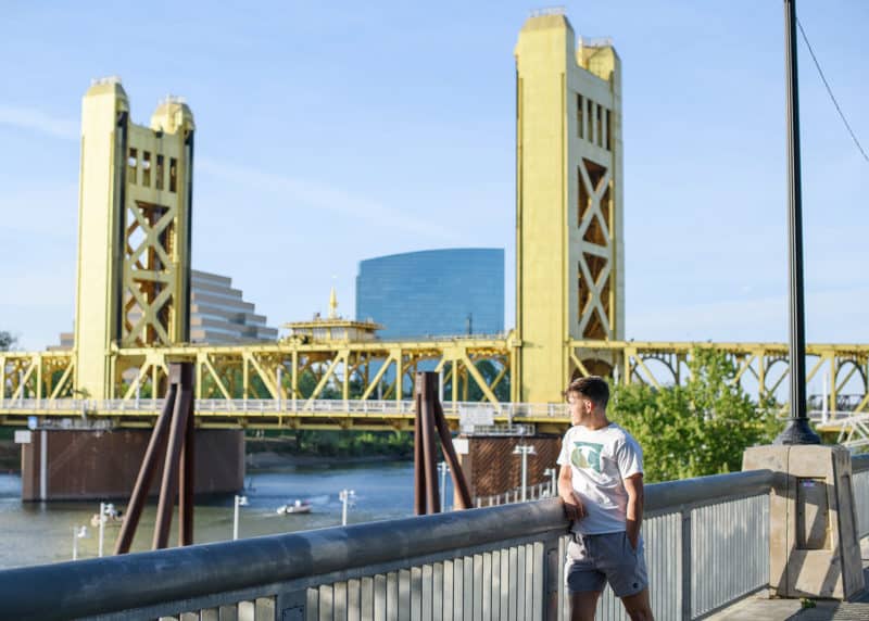 high school senior boy staring out at the tower bridge in downtown sacramento california