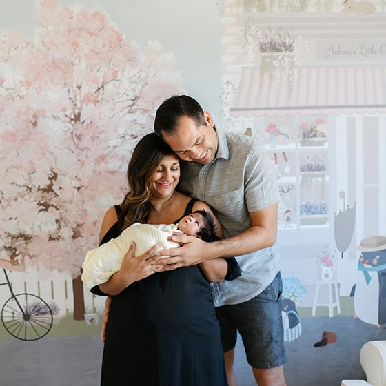 mom and dad with newborn girl in front of nursery mural