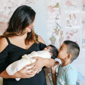 mom holding newborn baby girl with big brother kissing her on the head