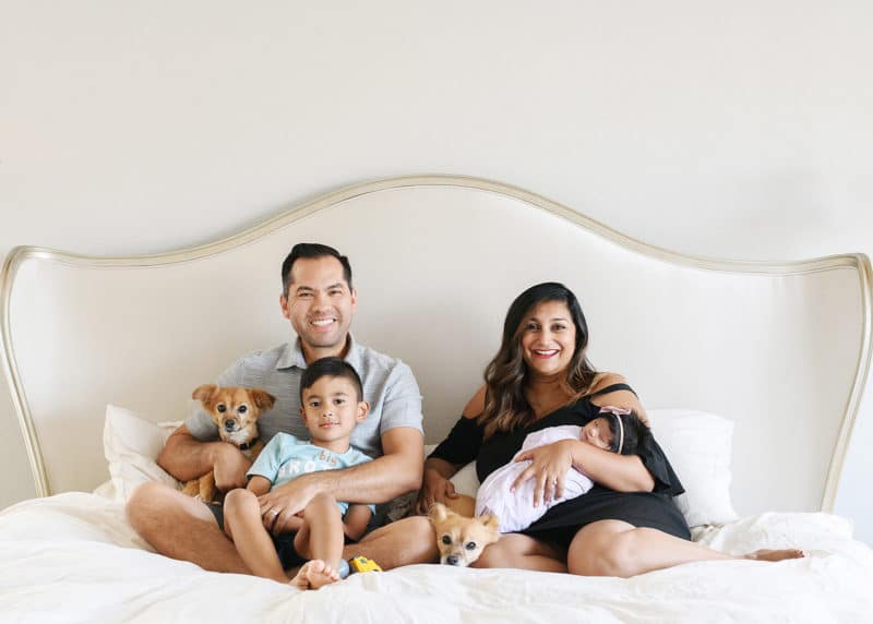mom and dad with newborn baby girl and young son sitting on the bed with the family dog