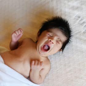 newborn baby girl yawning on bed at home session