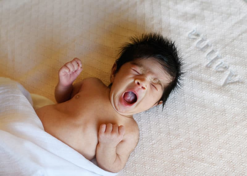 newborn baby girl yawning on bed at home session