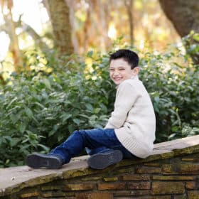 young boy giggling while sitting on a stone railing outside in natural light