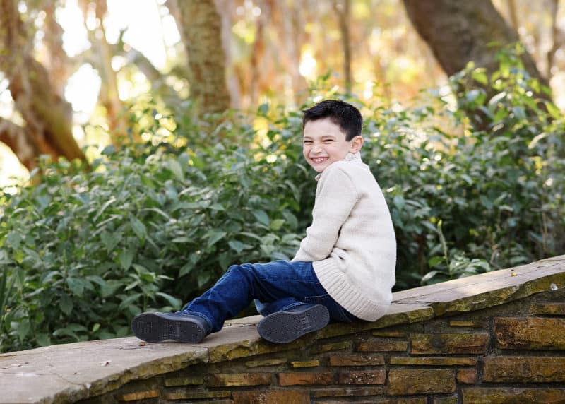 young boy giggling while sitting on a stone railing outside in natural light